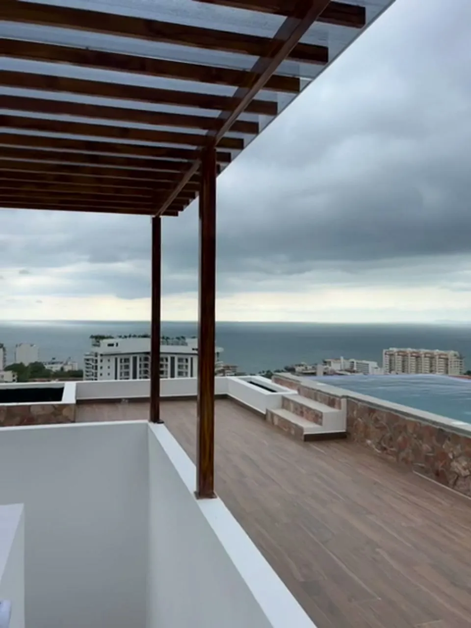 Pérgola de madera en la terraza frente a la alberca y la bahía